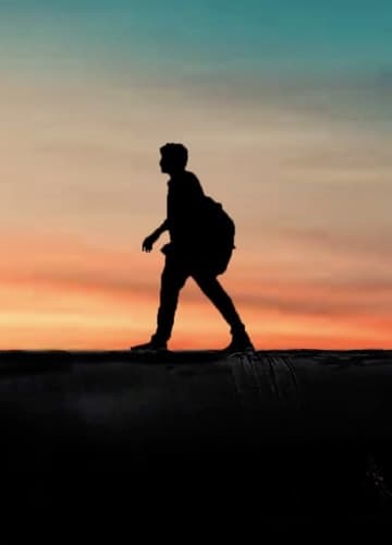A silhouette of a person walking against a colorful sunset sky.