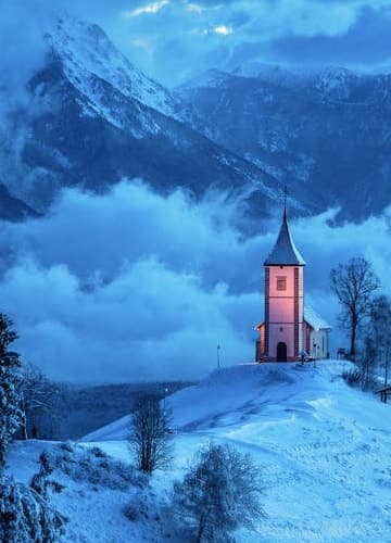 A snow-covered church with majestic mountains in the backdrop.