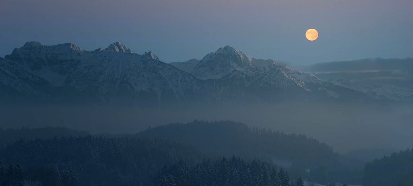 A serene full moon illuminates the majestic mountains in this captivating photo.