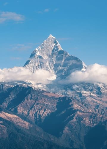A majestic mountain peak towering above clouds with a blue sky in the background.