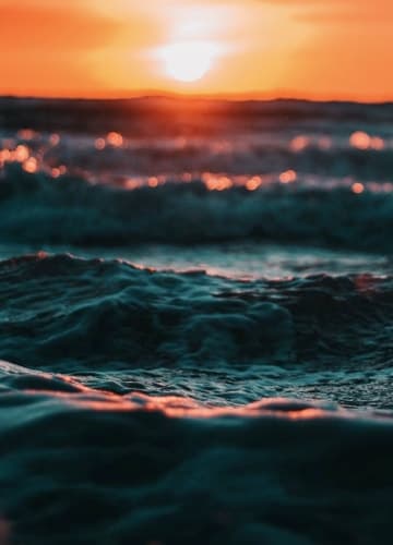 A breathtaking sunset over the ocean, casting a warm glow on the water and creating a serene atmosphere.